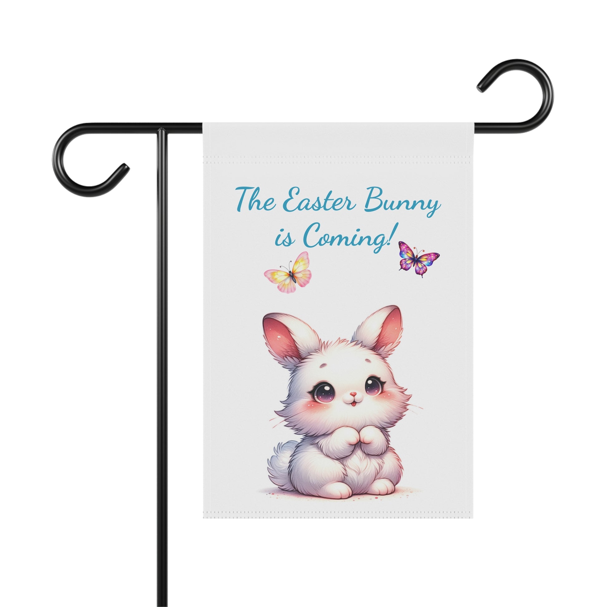 White garden flag with the text "The Easter Bunny is Coming!" in blue, an illustration of a cute white rabbit, and two colorful butterflies, displayed on a black metal garden flag stand.