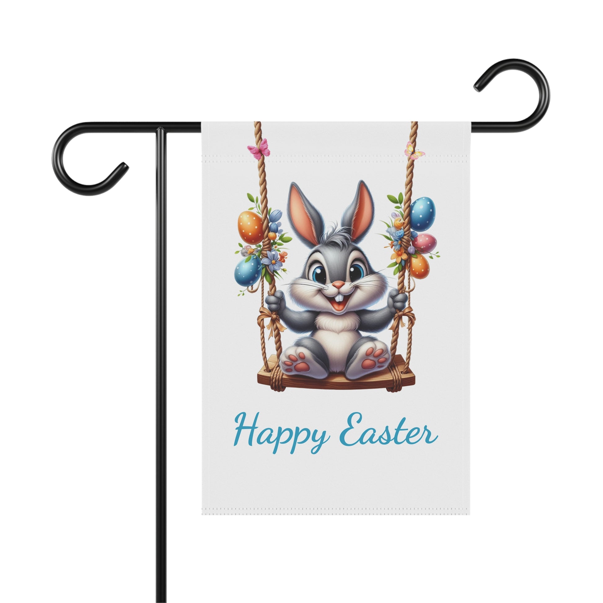 White garden flag with "Happy Easter" in blue text, featuring a cute gray cartoon bunny smiling and sitting on a rope swing, surrounded by colorful Easter eggs and small flowers. The flag is displayed on a black metal garden flag stand.