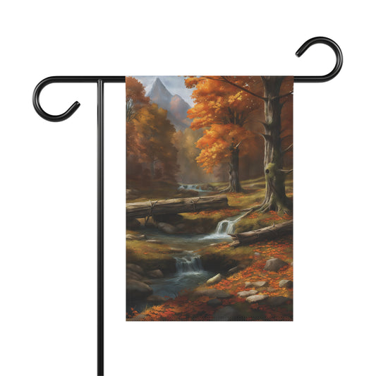 Garden flag depicting a scenic autumn forest landscape with a stream flowing through it, a log bridge spanning the stream, trees with orange and yellow fall foliage, and distant mountains. Fallen leaves are scattered on the ground.