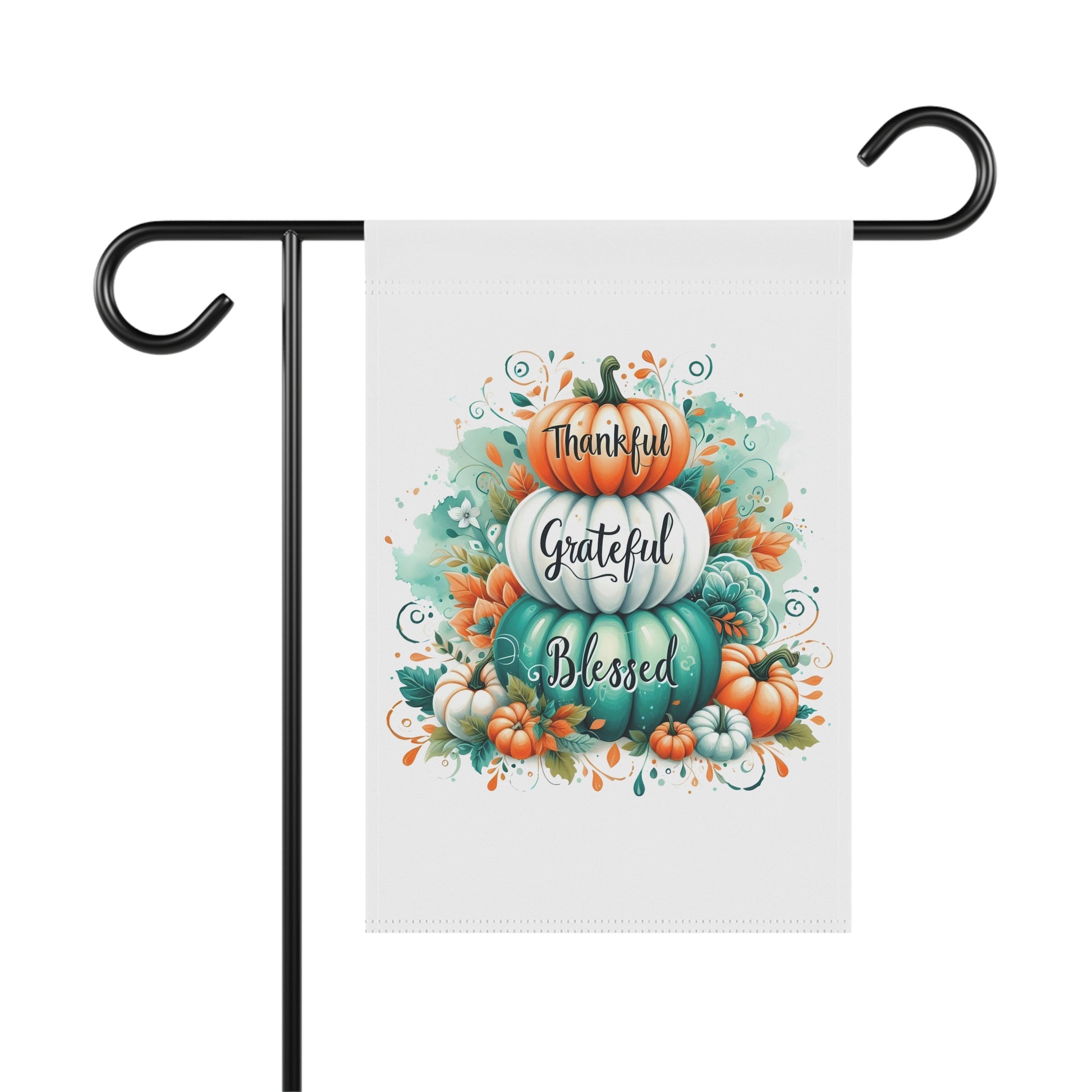 White garden flag with a stack of three pumpkins, colored orange, white, and teal, with the words "Thankful," "Grateful," and "Blessed" written on them. The pumpkins are surrounded by fall leaves and small pumpkins.