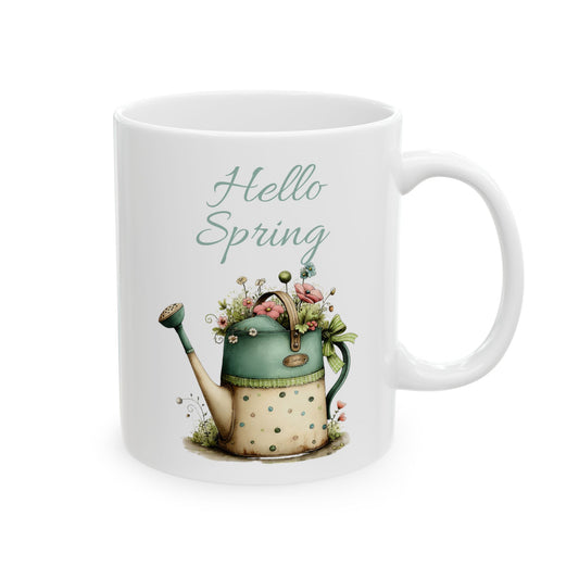 White ceramic coffee mug printed with sage green Hello Spring text above a vintage watering can filled with pastel flowers