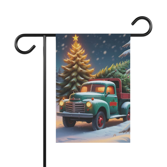 Garden flag with a vintage green pickup truck carrying evergreen trees in a snowy landscape, with a large lit Christmas tree and falling snow in the background.

