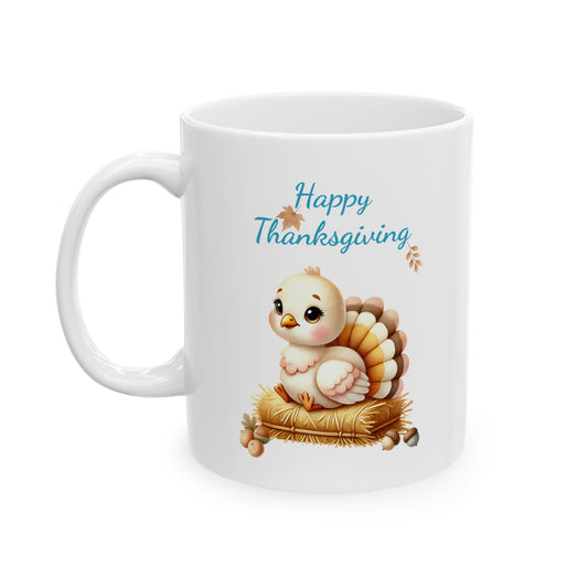A white ceramic coffee mug with a handle on the left. The front of the mug features an illustration of a cute, plump baby turkey with a white body and orange-brown layered tail feathers, sitting on a pile of yellow hay or straw. Small autumn leaves and orange berries are around the hay. Above the turkey, in blue script, are the words 'Happy Thanksgiving', with small brown leaves accompanying the text. 