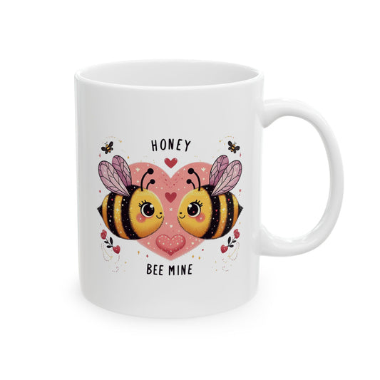 White ceramic coffee mug with a cartoon illustration of two adorable bees facing each other on a pink heart, and the text "Honey" and "Bee Mine."

