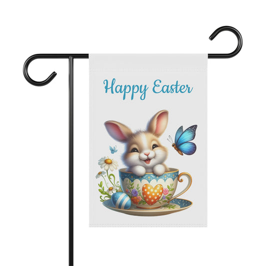 White garden flag with the text "Happy Easter" in blue, featuring a cute brown and white cartoon bunny in a floral teacup with a polka dot heart, surrounded by a blue butterfly, a striped blue Easter egg, and white daisies. The flag is displayed on a black metal garden flag stand.


