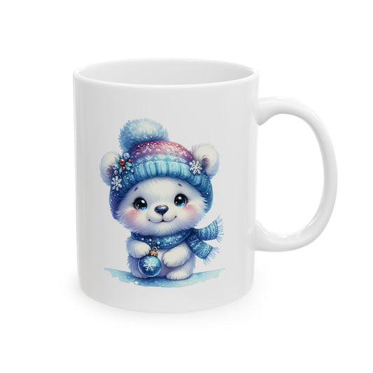 White ceramic coffee mug printed with an illustration of a cute white polar bear cub in a blue knit pom-pom hat and scarf holding a blue snowflake ornament