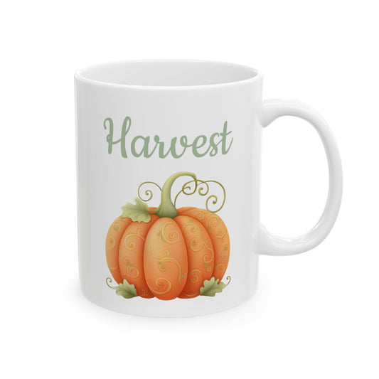 White ceramic mug featuring whimsical orange pumpkin illustration with green swirl details beneath sage green script text reading Harvest.
