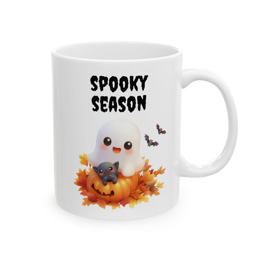 White ceramic mug featuring a cute ghost and black kitten sitting on a pumpkin among fall leaves beneath black text reading Spooky Season.