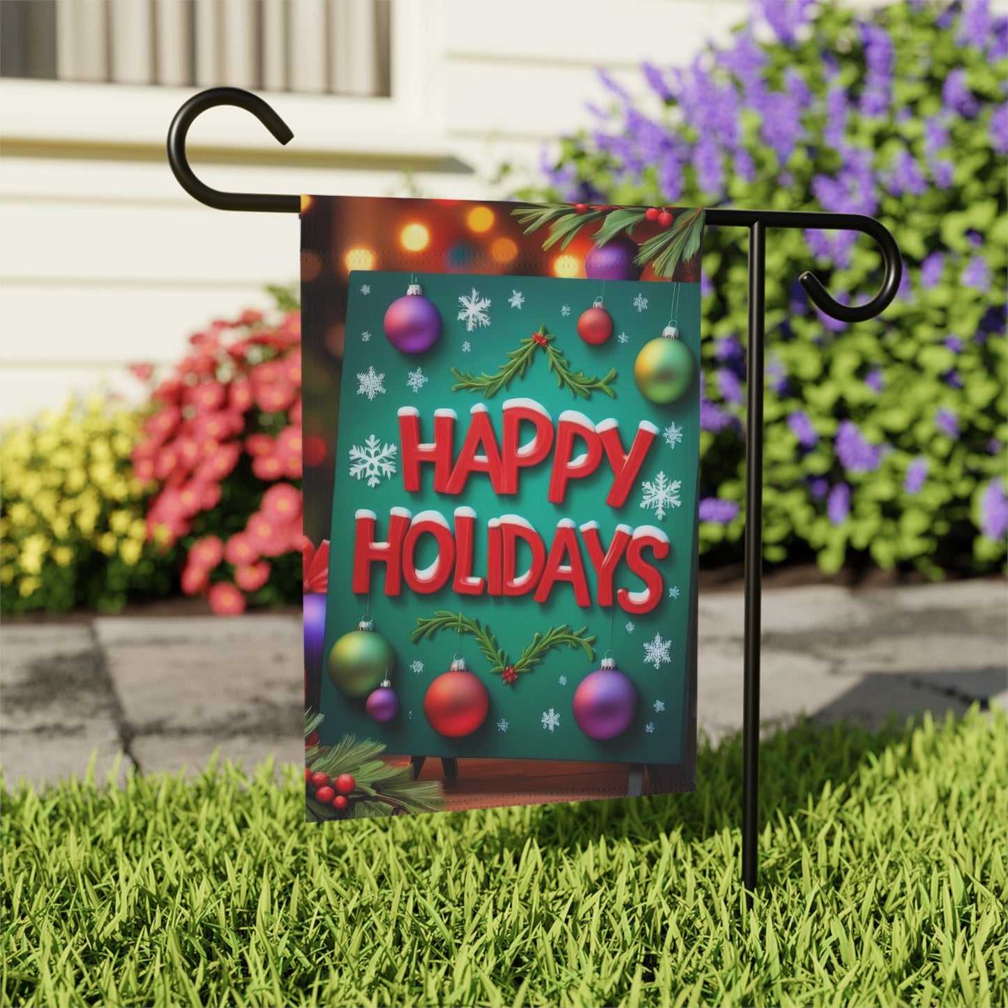Garden flag with a green sign that reads "Happy Holidays" in red bold letters, decorated with holly, snowflakes, and colorful Christmas ornaments, with blurred festive lights in the background.

