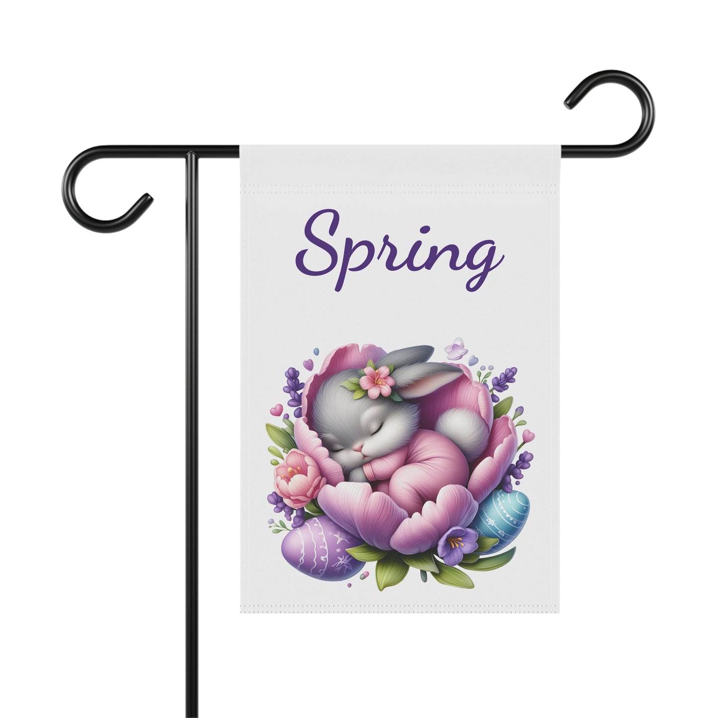 White garden flag displayed on a black metal pole, featuring a gray bunny in pink pajamas sleeping inside a large pink and purple flower, surrounded by decorated Easter eggs and small flowers, with the word "Spring" in purple script above.

