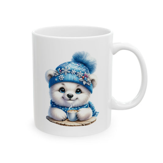 White ceramic coffee mug printed with an illustration of a cute white polar bear cub in a blue snowflake pom-pom beanie holding a cup of steaming coffee on a wooden slice