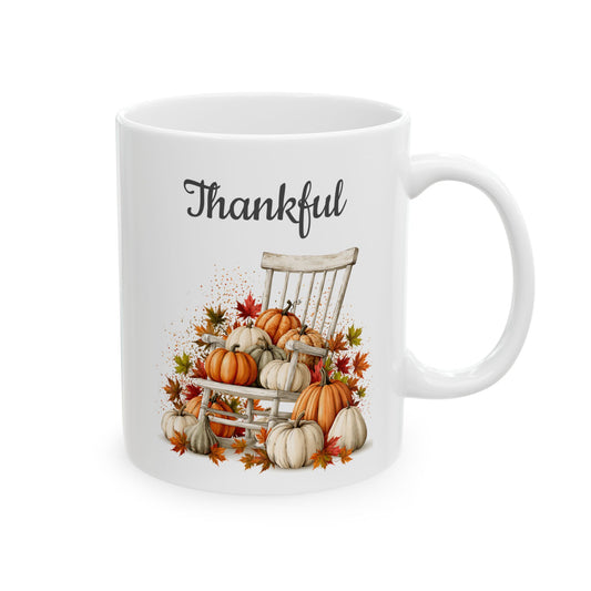 White ceramic coffee mug featuring a rustic white wooden chair surrounded by heirloom pumpkins, gourds, and autumn leaves beneath black script text reading Thankful.
