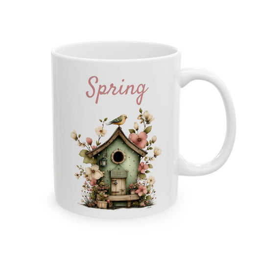 White ceramic coffee mug printed with dusty pink Spring text above a charming green birdhouse surrounded by floral blossoms and a songbird