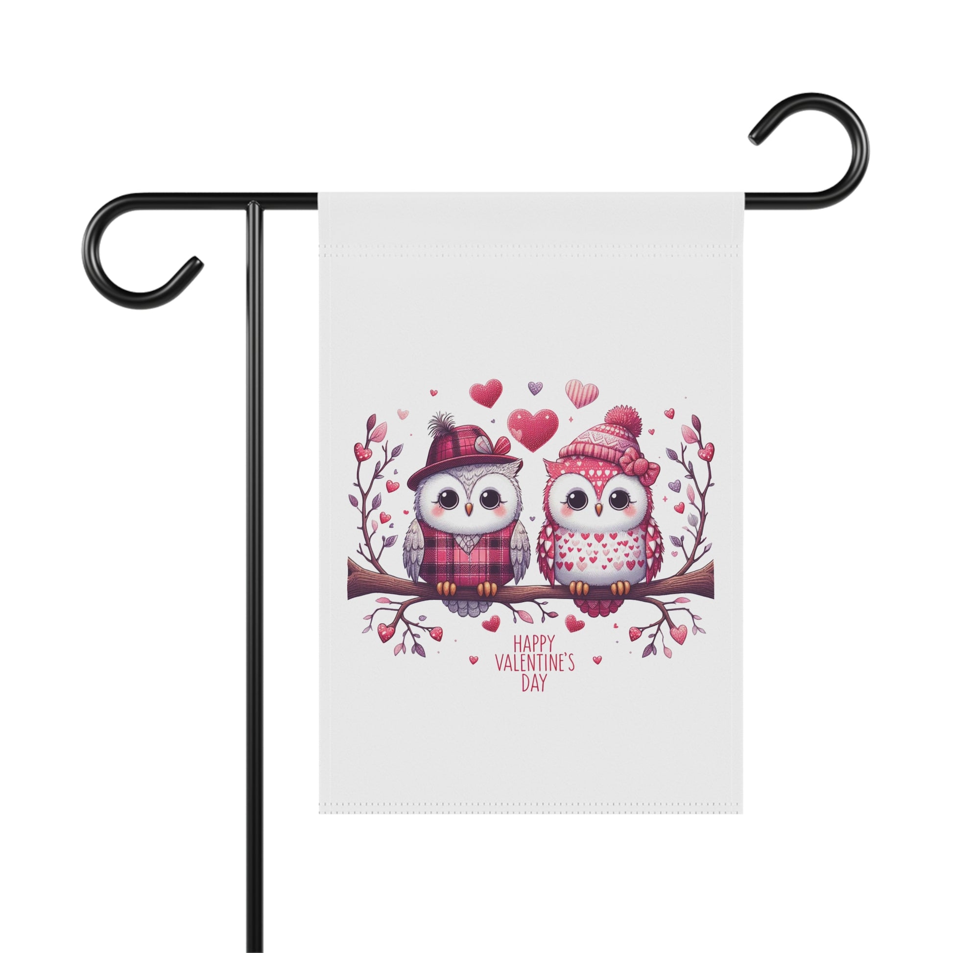 Happy Valentine's Day garden flag with a charming illustration of two cartoon owls wearing winter hats and scarves, sitting on a branch surrounded by hearts. The flag is hanging on a black metal holder.

