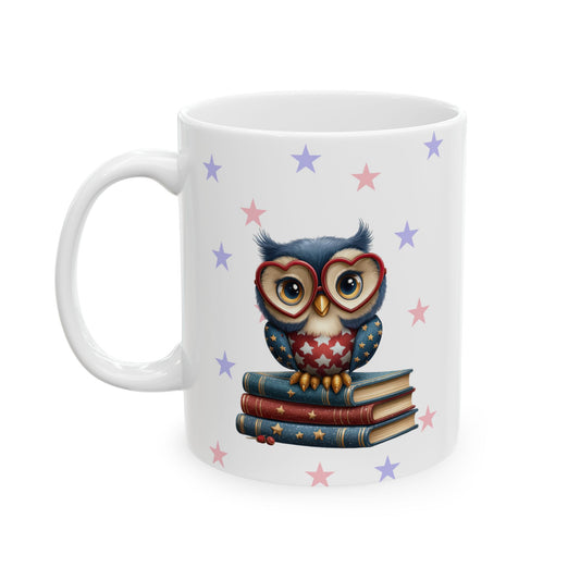 White ceramic coffee mug with a cute cartoon owl wearing red heart-shaped glasses and patriotic red, white, and blue chest feathers, sitting on a stack of books, with scattered pink and purple stars in the background