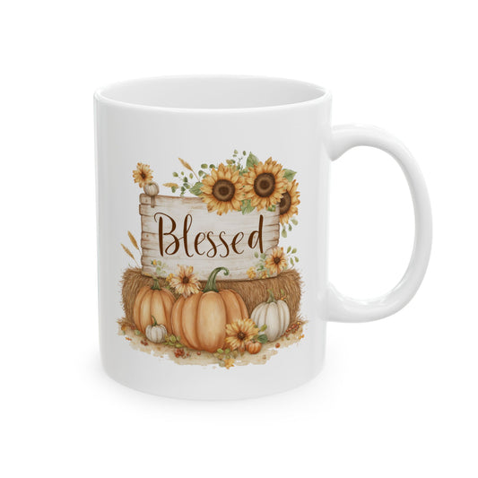 White ceramic coffee mug printed with brown Blessed script on a rustic wood sign framed by yellow sunflowers, a hay bale, and pumpkins