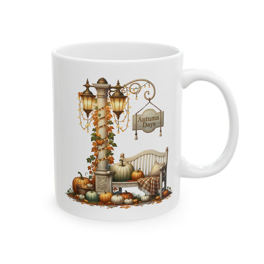 White ceramic coffee mug featuring a vintage autumn garden scene with a double lamppost, fairy lights, a bench with a plaid blanket, a sign that reads Autumn Days, and numerous pumpkins.

