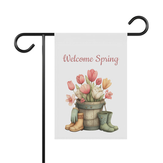 Spring garden flag featuring a wooden bucket filled with pink and yellow tulips flanked by gardening gloves, work boots, and green rain boots beneath pink script text reading Welcome Spring.