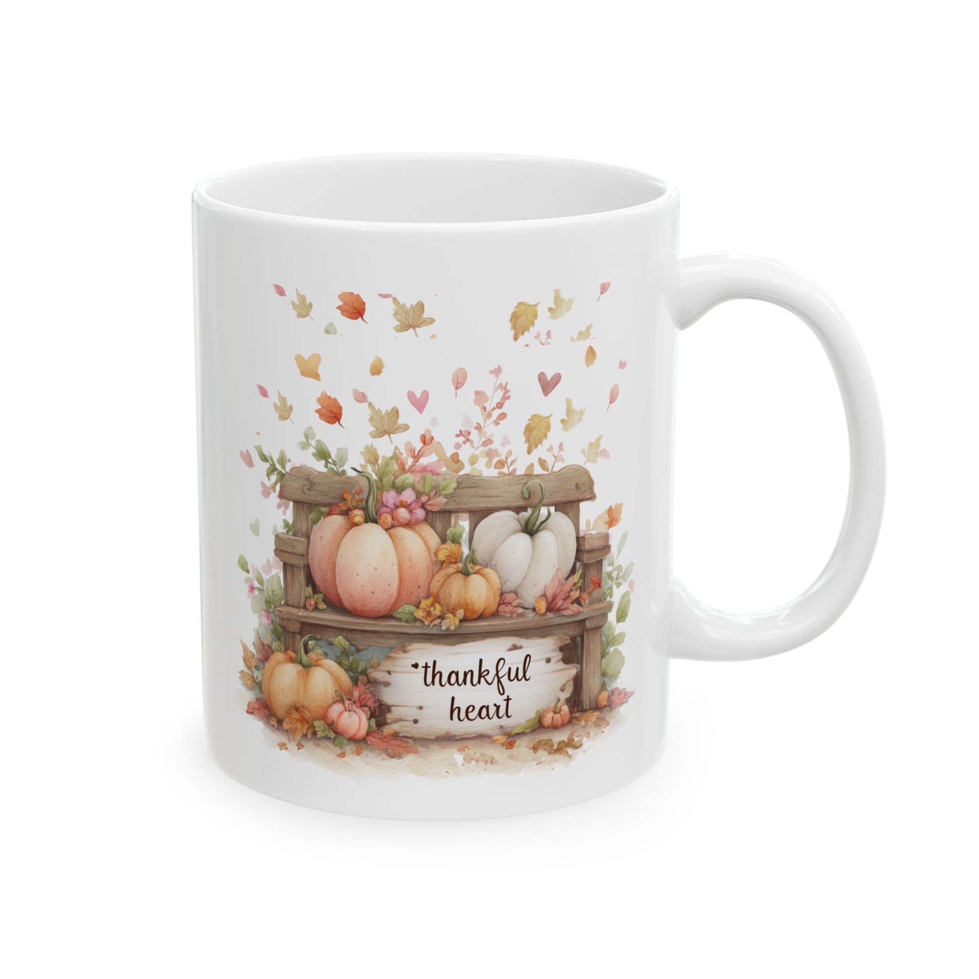 White ceramic coffee mug featuring a soft watercolor illustration of a rustic wooden bench filled with blush pink, orange, and white pumpkins, under drifting leaves and hearts, with a sign that reads thankful heart.
