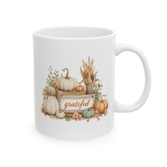 White ceramic coffee mug printed with orange Grateful script on a framed white sign surrounded by white pumpkins, a hay bale, green gourds, and Indian corn