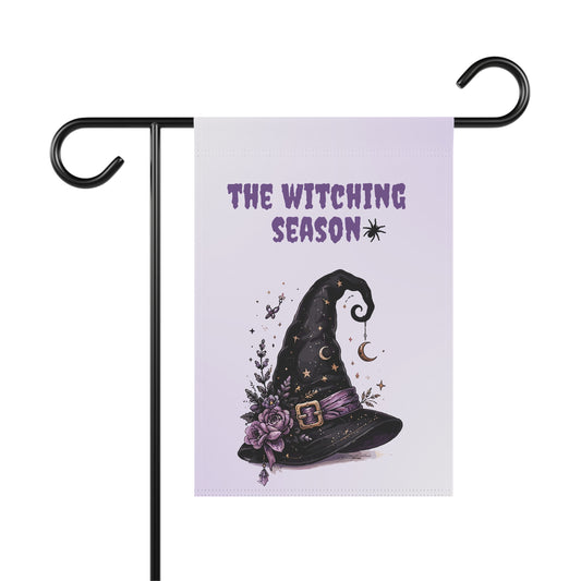 Black witch hat with purple flowers stars and crescent moons below The Witching Season text printed on a lavender Halloween garden flag, Lavender outdoor garden flag displayed on a metal pole featuring a celestial floral witch hat design and The Witching Season lettering, Floral witch hat Halloween yard flag for spooky outdoor front porch and garden decor