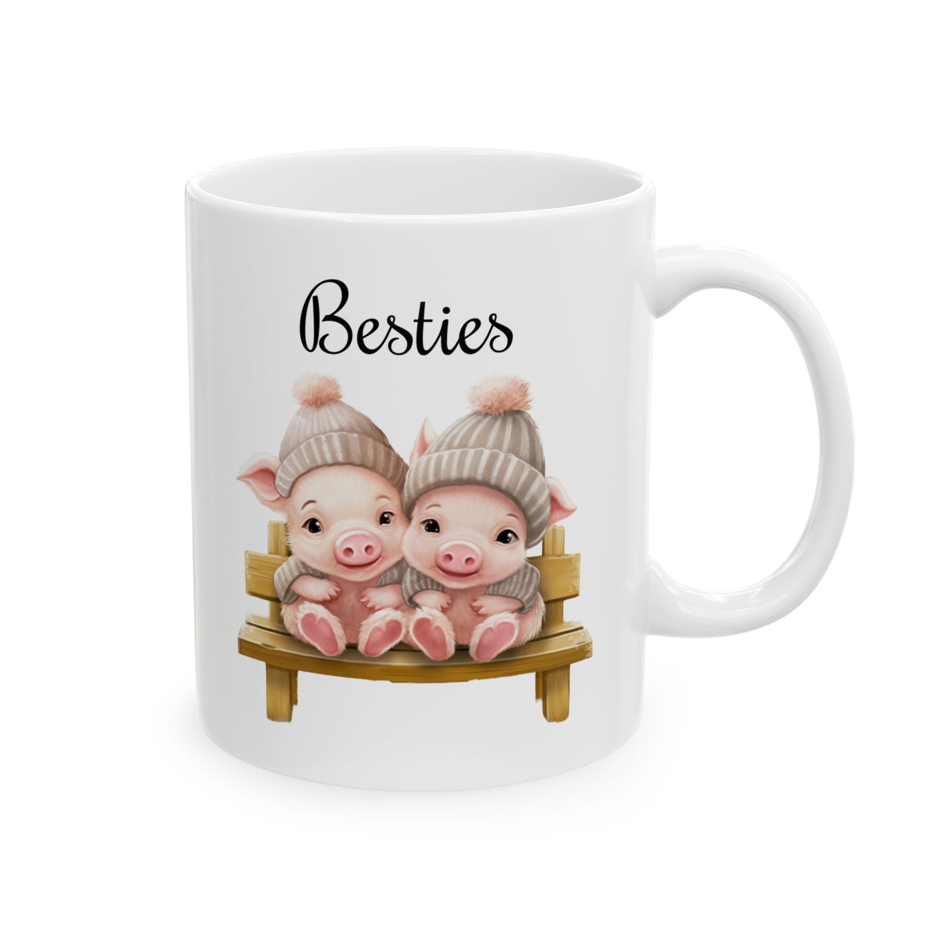 White ceramic coffee mug with a watercolor illustration of two cute cartoon piglets wearing gray knit hats, sitting together on a wooden bench, with black "Besties" text above.