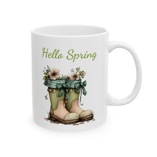 White ceramic coffee mug printed with green Hello Spring text above garden boots filled with soft spring flowers