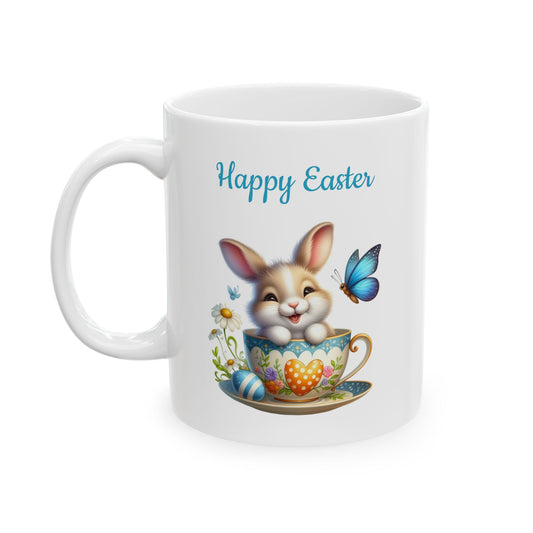 White ceramic mug with "Happy Easter" text, featuring a cute smiling cartoon bunny sitting in a light blue and orange patterned teacup, with a blue butterfly, daisies, and an Easter egg.

