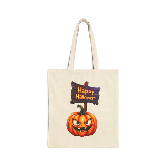 A cream-colored 100% cotton canvas tote bag featuring an illustration of a carved, spooky jack-o'-lantern with a wide grin next to a wooden sign that says "Happy Halloween."