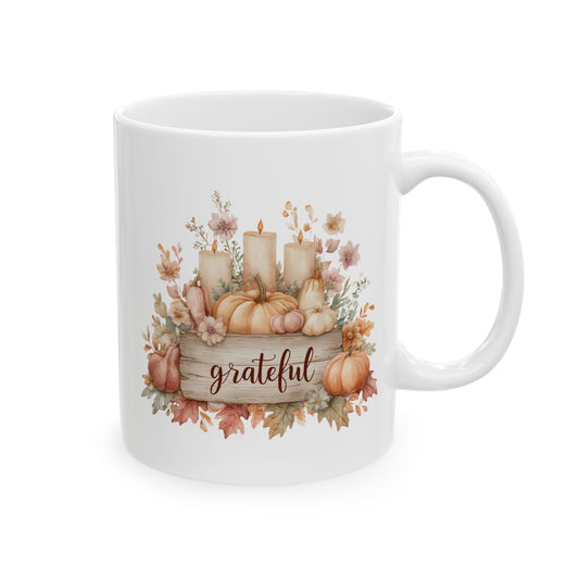 White ceramic coffee mug printed with brown Grateful script on a wooden sign topped with lit pillar candles, pumpkins, and autumn flowers