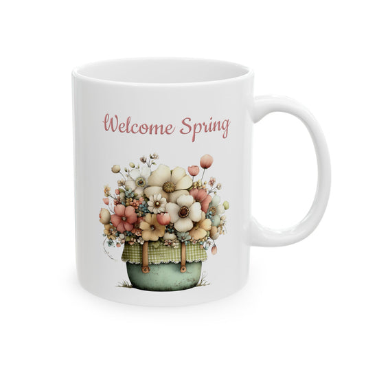 White ceramic coffee mug printed with soft pink Welcome Spring text above a charming floral basket overflowing with pastel flowers
