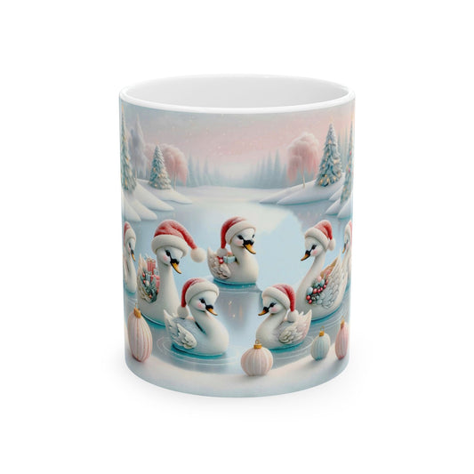 White ceramic coffee mug with a beautiful illustration of several white swans and cygnets, all wearing red Santa hats, swimming in a frozen pond surrounded by a snowy winter landscape with trees and decorative pink globes.

