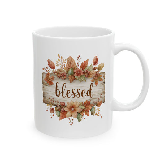 White ceramic coffee mug printed with brown Blessed script on a rustic wood plank framed by warm autumn leaves and berries