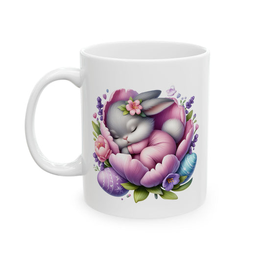 White ceramic mug with "Happy Easter" text, featuring a cute grey baby cartoon bunny sleeping peacefully inside a large pink and purple flower, adorned with smaller flowers and two decorated Easter eggs.

