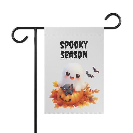 Cute friendly ghost sitting on a pumpkin with a small black cat surrounded by autumn leaves and bats below Spooky Season text printed on a white garden flag, White Halloween garden flag on a metal stand featuring cute ghost black cat and jack-o'-lantern artwork with Spooky Season text, Cute ghost and black cat garden flag for Halloween outdoor front porch and yard decor