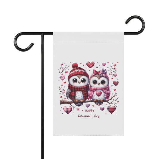 Happy Valentine's Day garden flag with a charming illustration of two cartoon owls wearing winter hats and scarves, sitting on a branch surrounded by hearts. The flag is hanging on a black metal holder.

