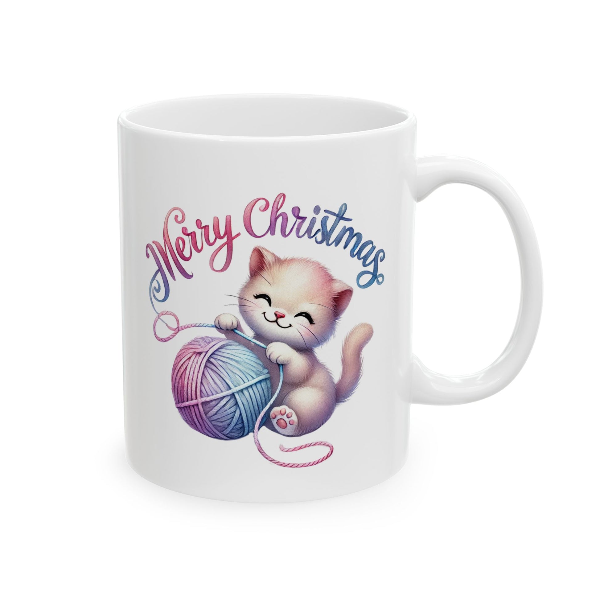 White ceramic coffee mug with a happy kitten playing with a pink and blue yarn ball and "Merry Christmas" text.