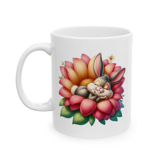 White ceramic mug with a cute grey cartoon bunny sleeping peacefully inside a large orange and pink blooming flower with green leaves.

