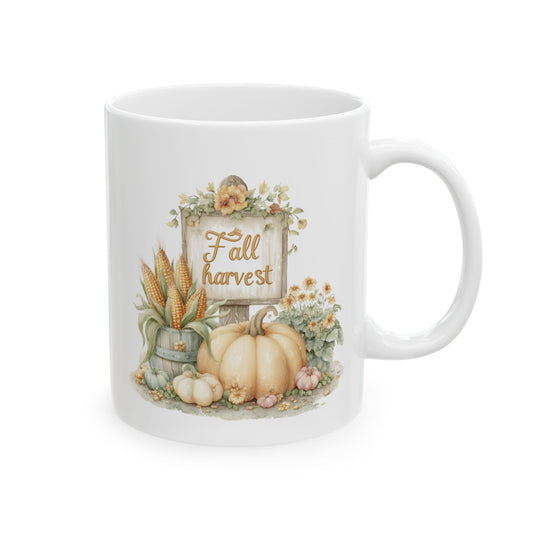 White ceramic coffee mug featuring a watercolor farmhouse illustration of a cream pumpkin, a bucket of field corn ears, and yellow flowers next to a wooden sign that reads Fall harvest.