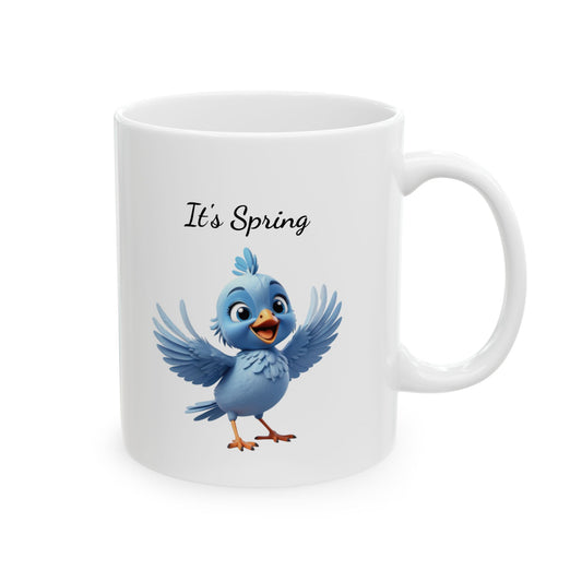 White ceramic coffee mug with a 3D-style illustration of a cute, cheerful blue cartoon bird with wide-open wings, and black text above reads "It's Spring!".