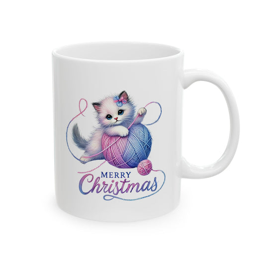 White ceramic coffee mug printed with a cute fluffy kitten playing with a pink and blue ball of yarn above Merry Christmas script