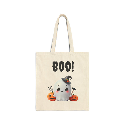 A cream-colored canvas tote bag featuring an illustration of a cute white ghost wearing a witch's hat and sitting between two carved pumpkins. The word "BOO!" is printed in a spooky font above the ghost.