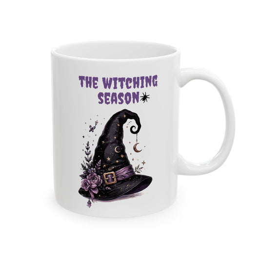 White ceramic mug featuring an illustrated witch hat with purple flowers, stars, and crescent moons beneath purple text reading The Witching Season.
