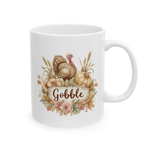 White ceramic coffee mug printed with brown Gobble script on a rustic wood plaque topped with a turkey, pumpkins, wheat, and fall flowers