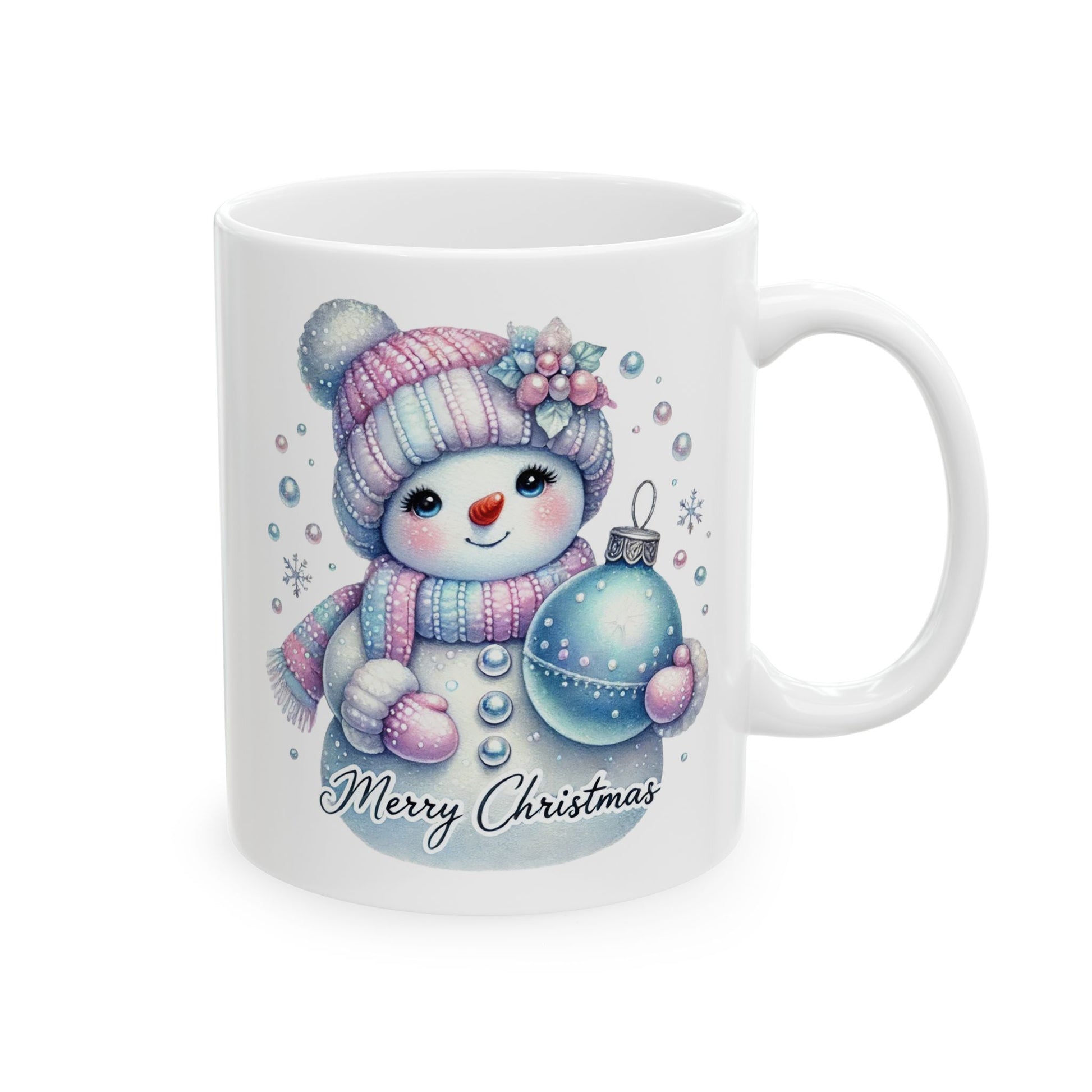 White ceramic coffee mug with a watercolor illustration of a cute snowman wearing a pink and blue striped hat and scarf, holding a blue Christmas ornament, with "Merry Christmas" written below.
