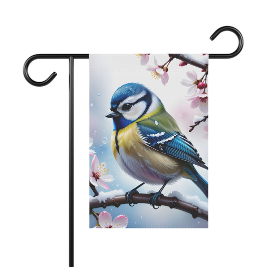 A garden flag featuring a realistic illustration of a blue tit bird perched on a snowy branch with pink cherry blossoms.

