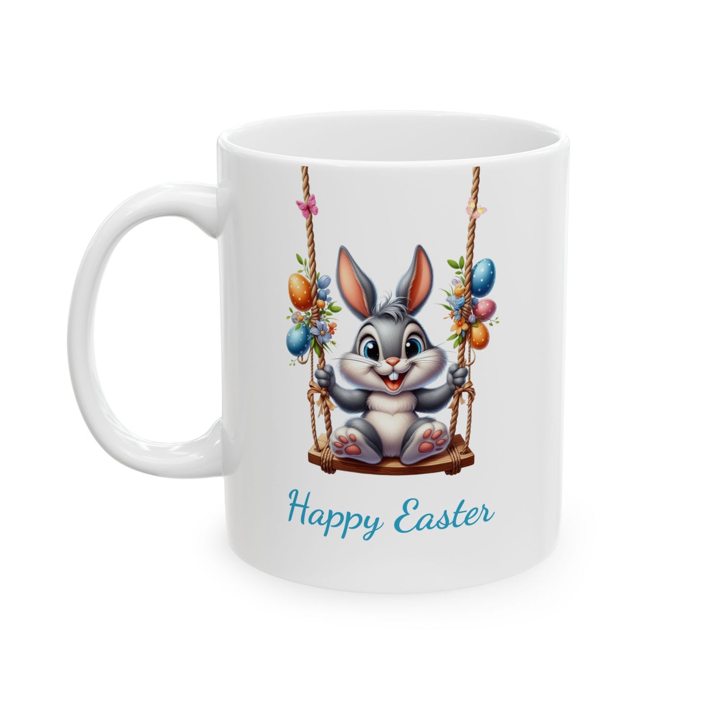 White ceramic mug with "Happy Easter" text, featuring a cute grey cartoon bunny smiling while sitting on a wooden swing decorated with Easter eggs and flowers.

