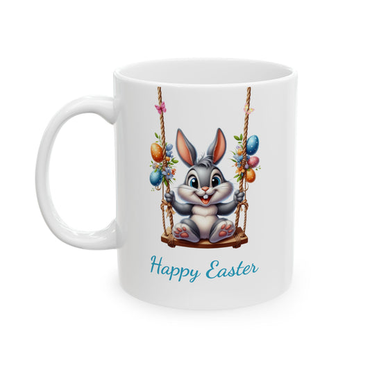 White ceramic mug with "Happy Easter" text, featuring a cute grey cartoon bunny smiling while sitting on a wooden swing decorated with Easter eggs and flowers.

