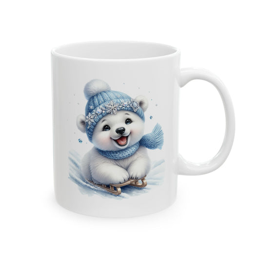 White ceramic coffee mug printed with an illustration of a cheerful white polar bear cub wearing a blue knit beanie and scarf riding a wooden sled in the snow