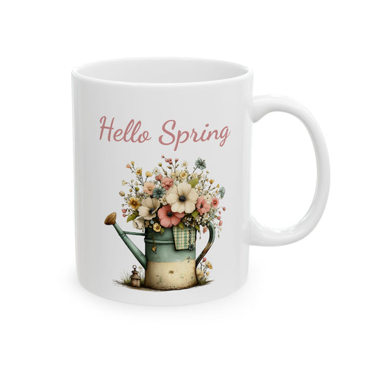 White ceramic coffee mug printed with dusty pink Hello Spring text above a rustic watering can overflowing with colorful wildflower blossoms